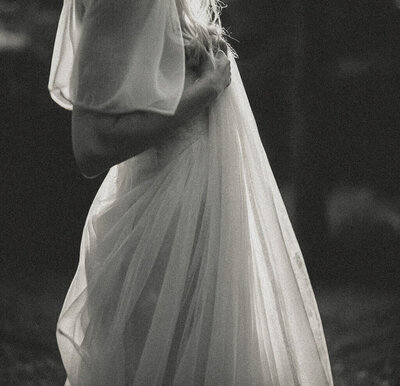 Black and white photo of a person in a sheer, flowing dress holding the fabric near their chest, with only their torso and arms visible—a striking visual perfect for Sweet Pea Ink Creative’s brand design inspiration.