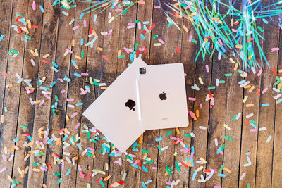 Two iPads with Apple logos face down on a wooden surface covered in colorful confetti, ready to showcase your Showit design services.