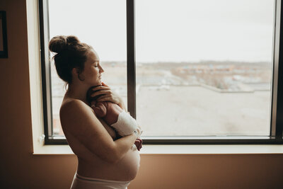Maternity session photo of new mother holding newborn i front of window