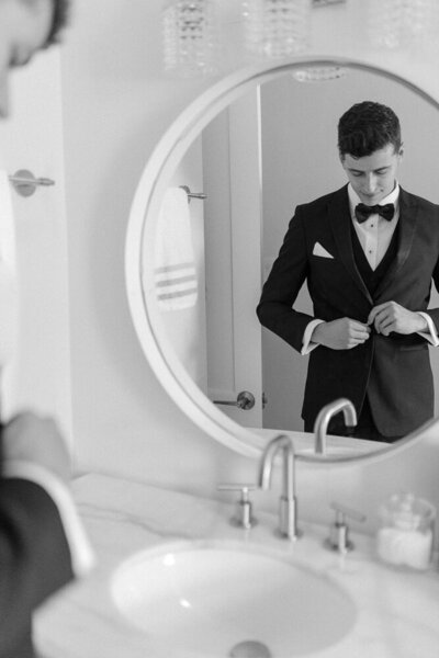 a mirror reflection showing a groom buttoning his suit jacket