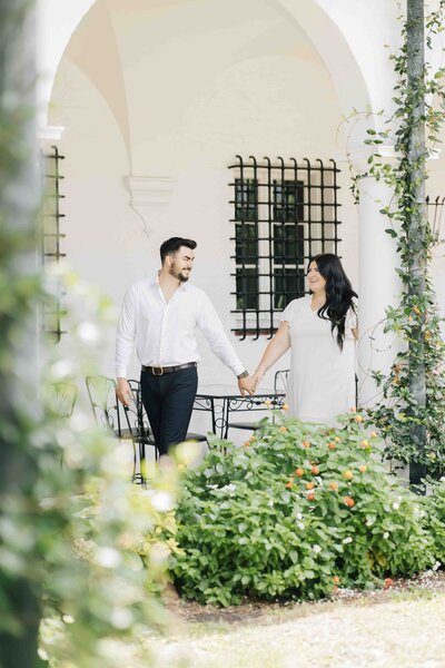 an engaged couple walking in a garden while holding hands