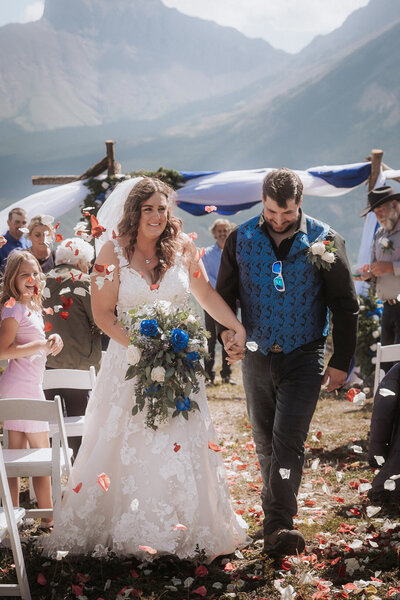 A bride and groom walk up the aisle after getting married, being showered in flower petals.