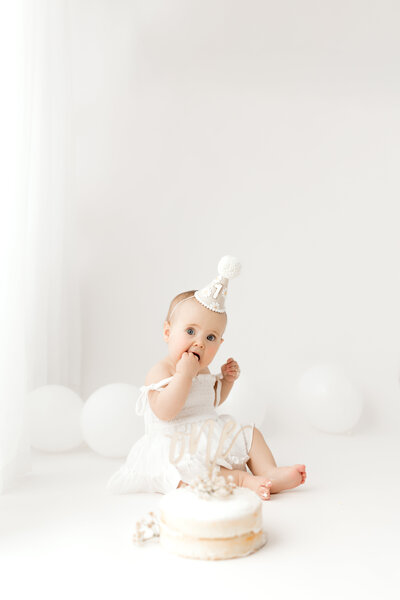 A one year old eating cake on a white background during her in studio cake smash photography session.