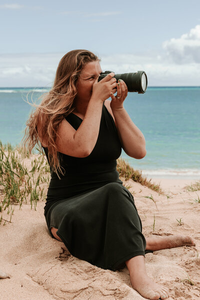 Sierra the owner of Sierra Bertini sitting on a beach in Maui in a black dress taking photos of clients