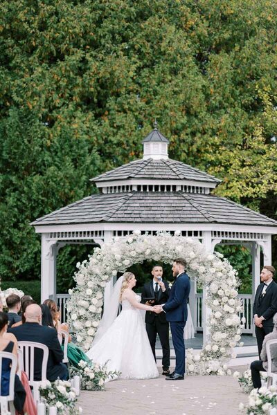 Bride and groom exchanging vows under a floral arch at Deer Creek – wedding photography by Ontario-based photographer