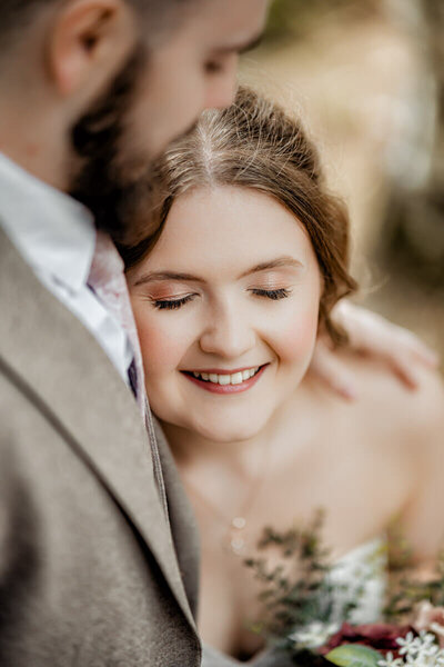A joyful bride smiling with eyes closed as she leans into her groom during a soft and emotional wedding moment, captured by a UK wedding photographer.