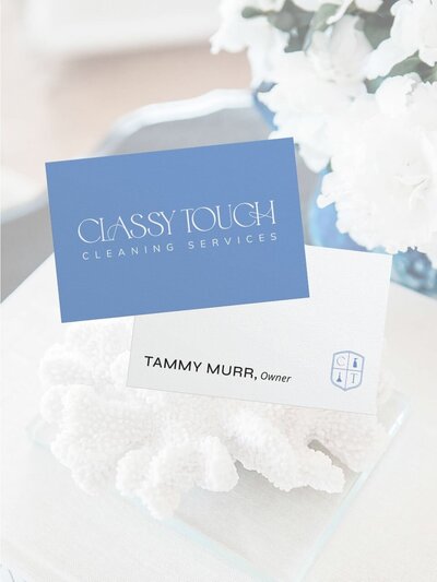 Stacked business cards for Classy Touch Cleaning—one in dusty blue with the full logo, and the other in white displaying owner Tammy Murr’s name with the CT crest icon—styled on a soft white tabletop with coral decor.
