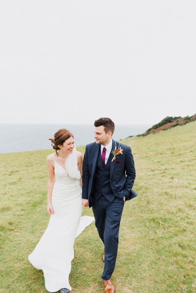 A couple walking along the coast in a field on their wedding day taken by Cornwall Wedding Photographer and Devon Wedding Photographer Liberty Pearl