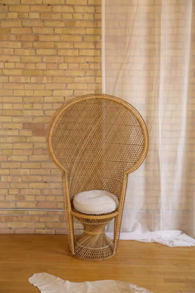 A peacock chair with a white cushion set up against a brick wall.