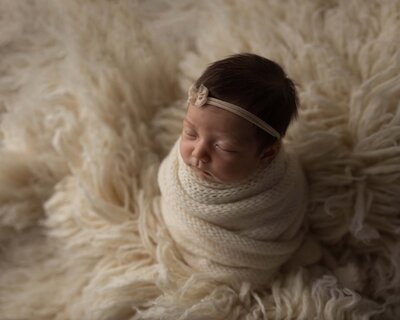 Newborn baby wrapped in a cream wrap sleeping sitting up with a bow in her hair