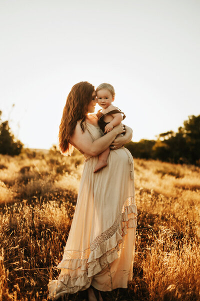 Pregnant mom holding her toddler in a field at golden hour.