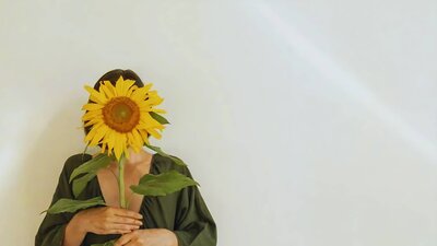 Symbolisk bild av en person som döljer sitt ansikte bakom en solros – en visuell metafor för medberoende och hur vi ofta gömmer vårt verkliga jag för att passa in eller behaga andra.