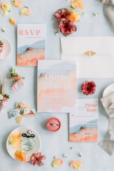 Wedding invitation and wedding detail flatlay in dusty blue, peach, and coral pink
