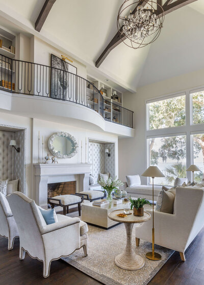 A living room with exposed woods beams, fire place, and a balcony over looking.