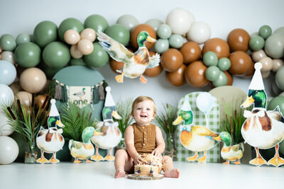 Boy celebrating his first birthday with a Mallard Duck-themed cake smash set featuring green tones and custom props.