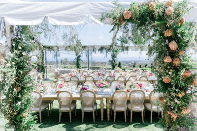 Luxurious dinner party at Montecito estate with view of Santa Barbara under a clear-top tent with greenery floral installations and chandeliers hanging over tables