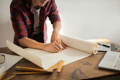 Contractor drafting home renovation plans on a table with rolled blueprints and tools.