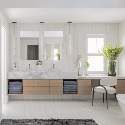 Wellesley primary bathroom with white walls, light wood vanity drawers, and greenery in a glass vase for a serene, modern look