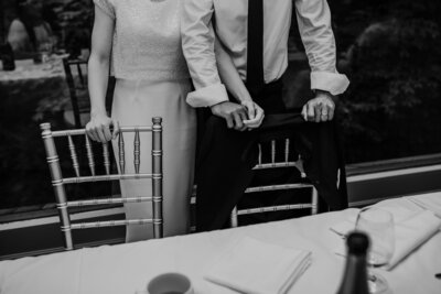 Bride and groom are walking away from the camera at Prim and Peony Event Co., just outside of London, ON. The image is captured in black and white and of the backs of the bride and groom. The bride is holding her flower and the groom is helping hold the bride's train. Captured by Ashlee Ellison, top London, ON wedding photographer.