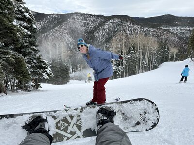 The professional family photo sessions in Albuquerque with this dynamic image of skiing in the snow. The skier is dressed in a blue hat with goggles, red pants, and a winter jacket, set against a backdrop of snow-covered trees.