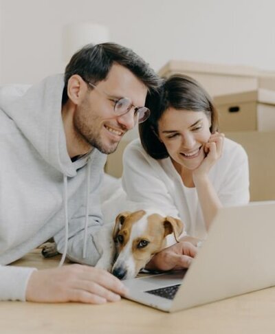 Happy couple using their laptop can describe couples working through It's Okay To Stay online coaching programs for couples in the aftermath of infidelity. Heal from infidelity with our experts.