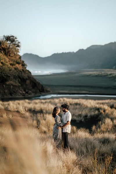 Keerthana and Suraj walking hand in hand on grassy coastal hills in Auckland during engagement photoshoot by Zanthe Vorsatz.