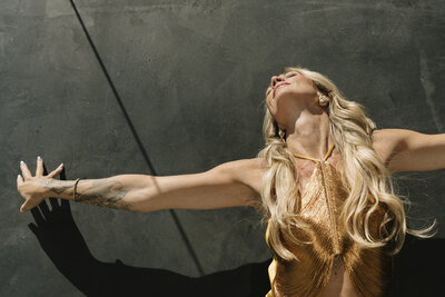 Aine Rock in a gold shirt with her arms out  stretched 