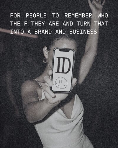 A female at a club in a white dress with her hair in a slick back pony tail holding up her phone that says ID with a smile face.