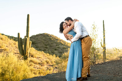 husband and wife, owner of Cactus & Pine Photography, hugging in a desert view at sunset
