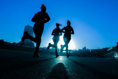 Three runners with a blue background running at sunset