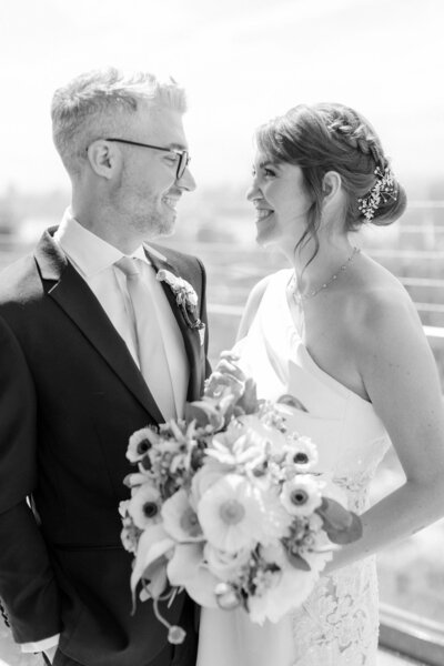 Black and white image of bride and groom gazing into each others eyes on city rooftop