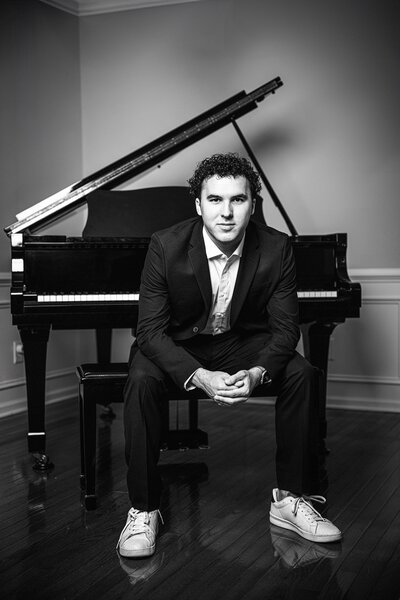 black and white portrait of a charlotte area senior posing with his piano wearing a suite 