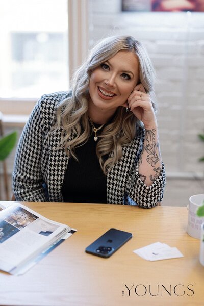 Jazmin leans her elbow on the table in front of her. On the table in front of her lies her phone, a wedding magazine, and Luna & Co Wedding Planners business cards. This woman has been at work. 