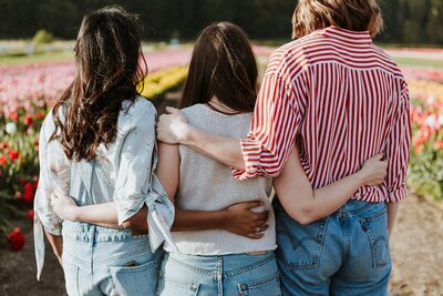 A diverse group of three women sitting together in a vibrant tulip field, highlighting community and support.