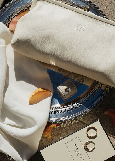 designer bridal clutch made of white leather laying on a silver plater featuring the bride and grooms wedding rings