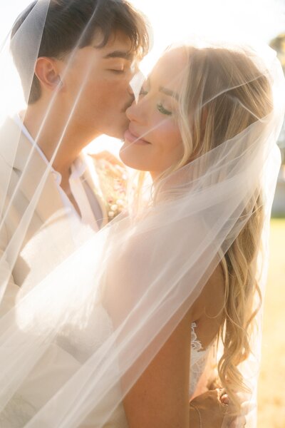 Warm, sunset portrait of bride and groom under veil at Nashville wedding