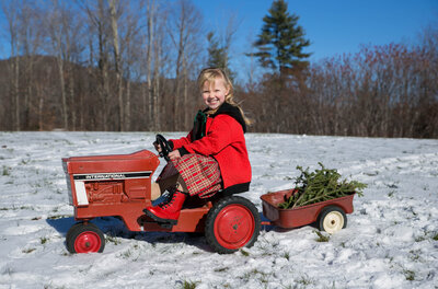 Blonde in red coat riding a toy tractor | Family Photo