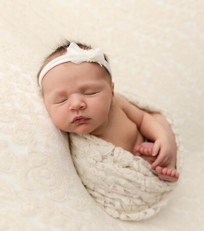Newborn portrait of a baby in womb pose wrapped in a cream pattern warp