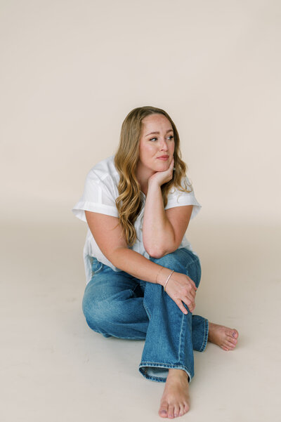 Courtney Paige sitting on the floor in a casual studio setting, resting her chin on her hand.