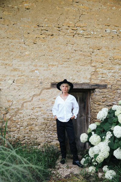 Sasha Armstrong standing in front of distressed brick wall and white hydrangas