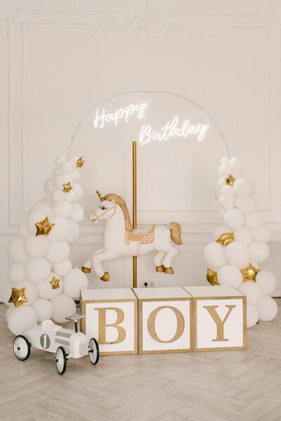 Decor vintage minimaliste pour un petit garçon avec ballons blancs et dorés, cheval et cubes en bois, et petite voiture ancienne.  Organisation d'anniversaire par un event planner.