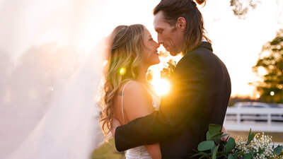 The bride and groom embrace in a tender kiss at sunset, surrounded by a beautiful, golden hour sky.