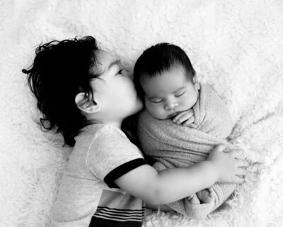 Mother is looking at her youngest son, who is held by his father, lovingly while the oldest boy is looking at the camera with a smile