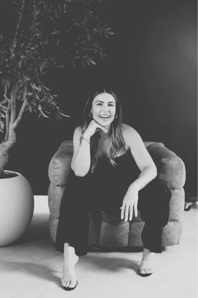 Natalie Bernacchi sitting confidently in a tan chair, smiling and grounded—embodying the bold energy of holistic mentorship