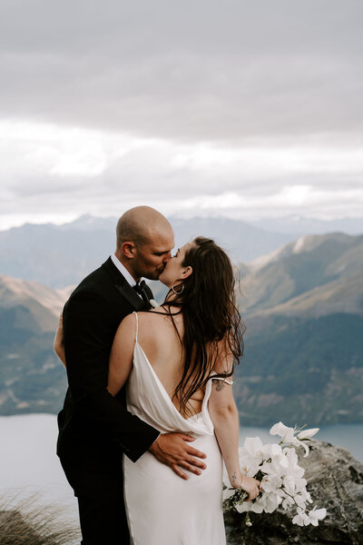 The Lovers Elopement Co - couple kiss on top of mountain, heli wedding