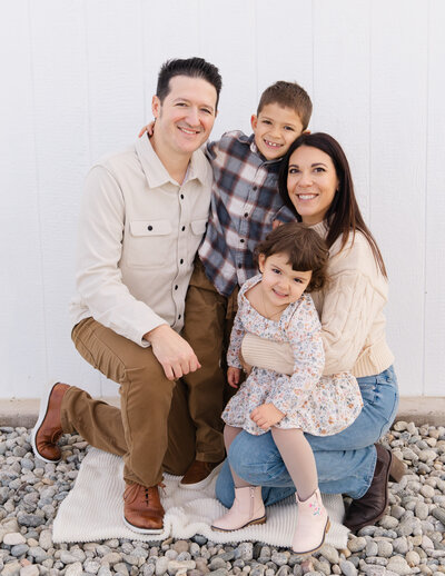 Family of four kneeling together sharing laughter and cuddles during a relaxed outdoor portrait session by Fort Collins portrait photographer Avenir Photo Co.