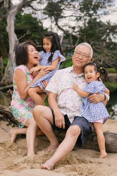Grandparents with their two young granddaughters laugh on the beach.