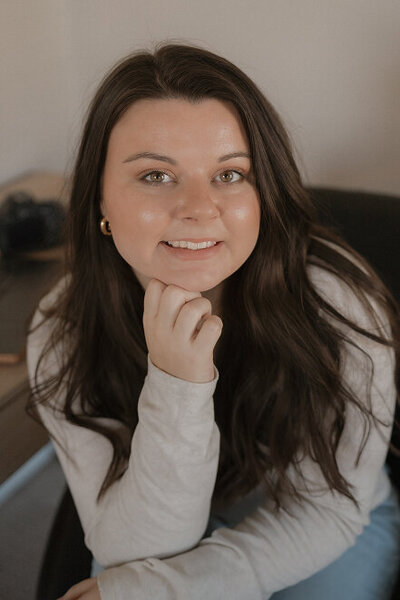 A photo of Michaela smiling up at the camera with her chin resting on her hand.