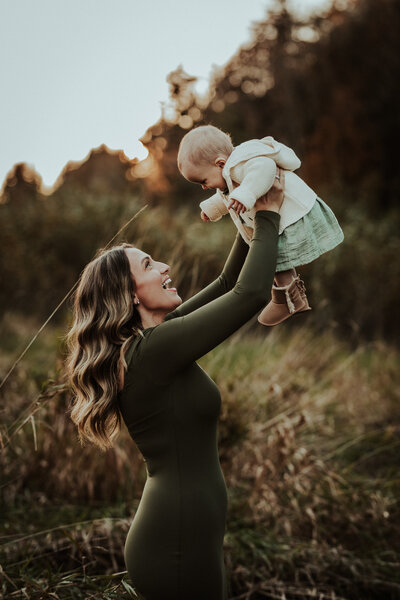 Mom and dad hold daughters while snuggling and kissing them in front of yellow flowes and trees