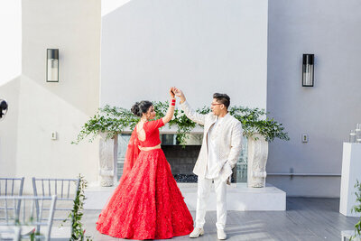 A couple dances in front of the modern fireplace at SoHo63, a Chandler wedding and event venue. The bride wears a bright red lehenga, and the groom is dressed in a white embroidered sherwani, creating a striking and joyful scene full of cultural celebration.